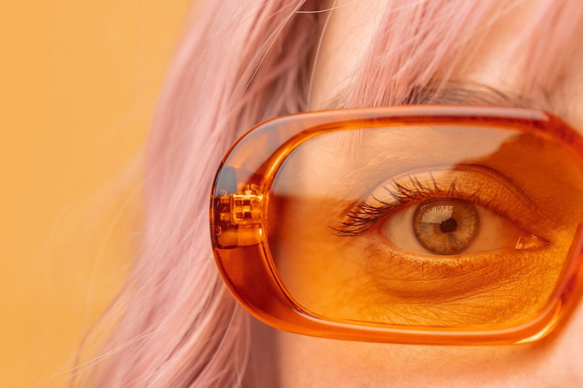 A woman wearing orange-lens sunglasses against a yellow background