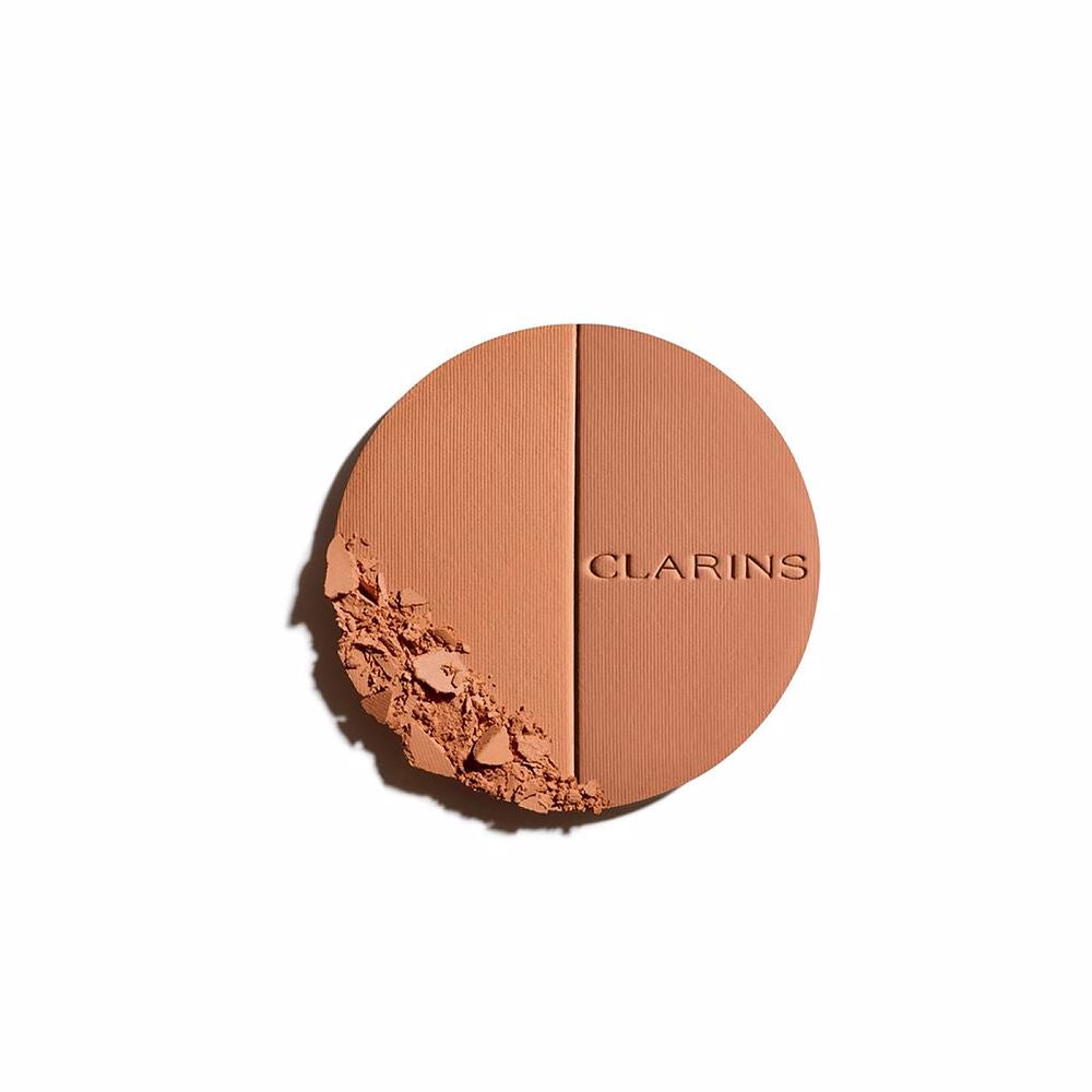 Clarins Round orange compact powder case with metallic rim, embossed brand name, minimalist metal/plastic finish